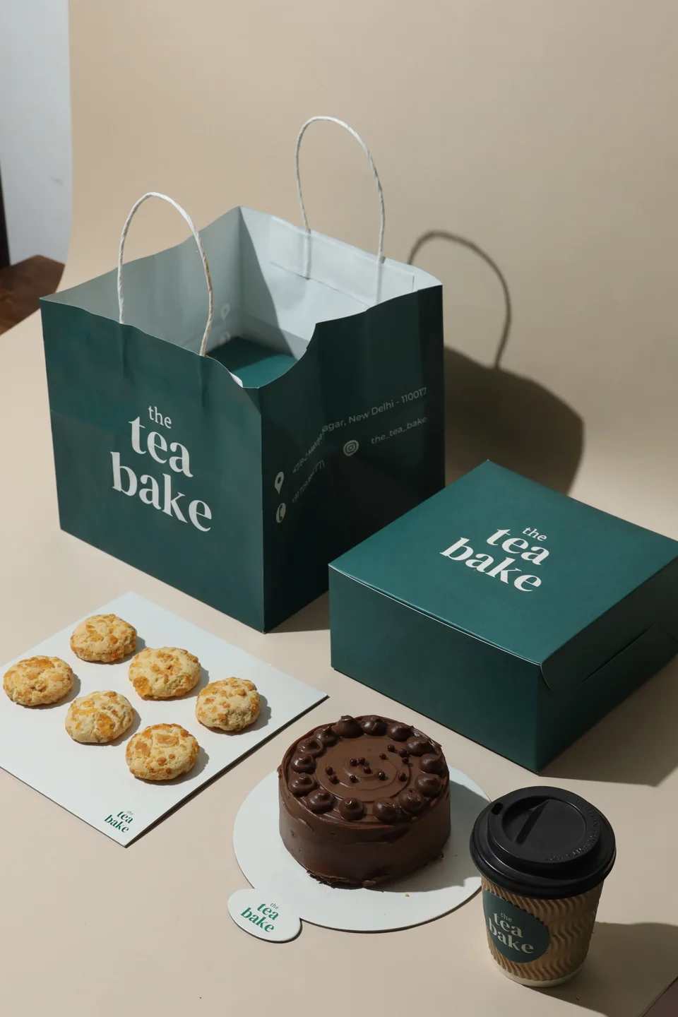 The Tea Bake branded box and matching paper bag beside a cake and cup