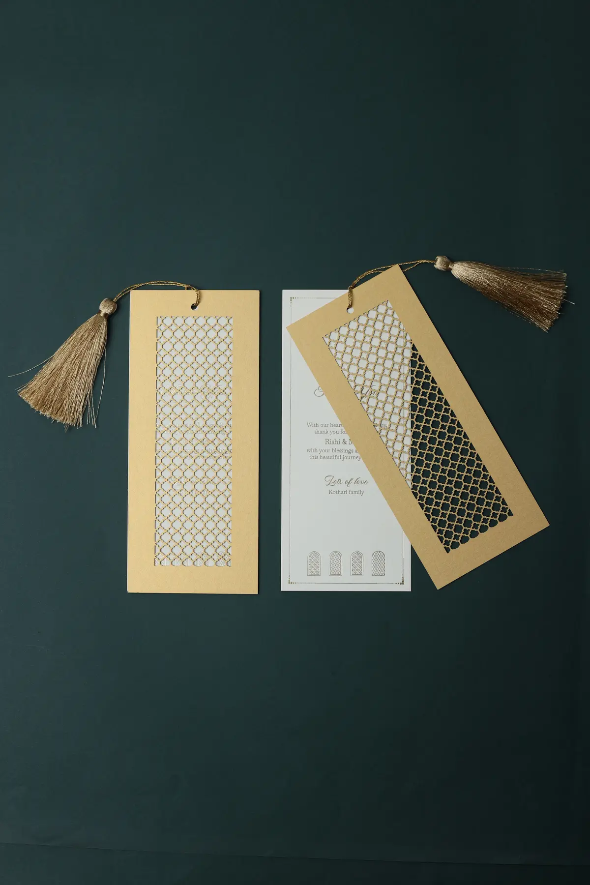 Gold cutwork invitation cards with tassels on a deep green background