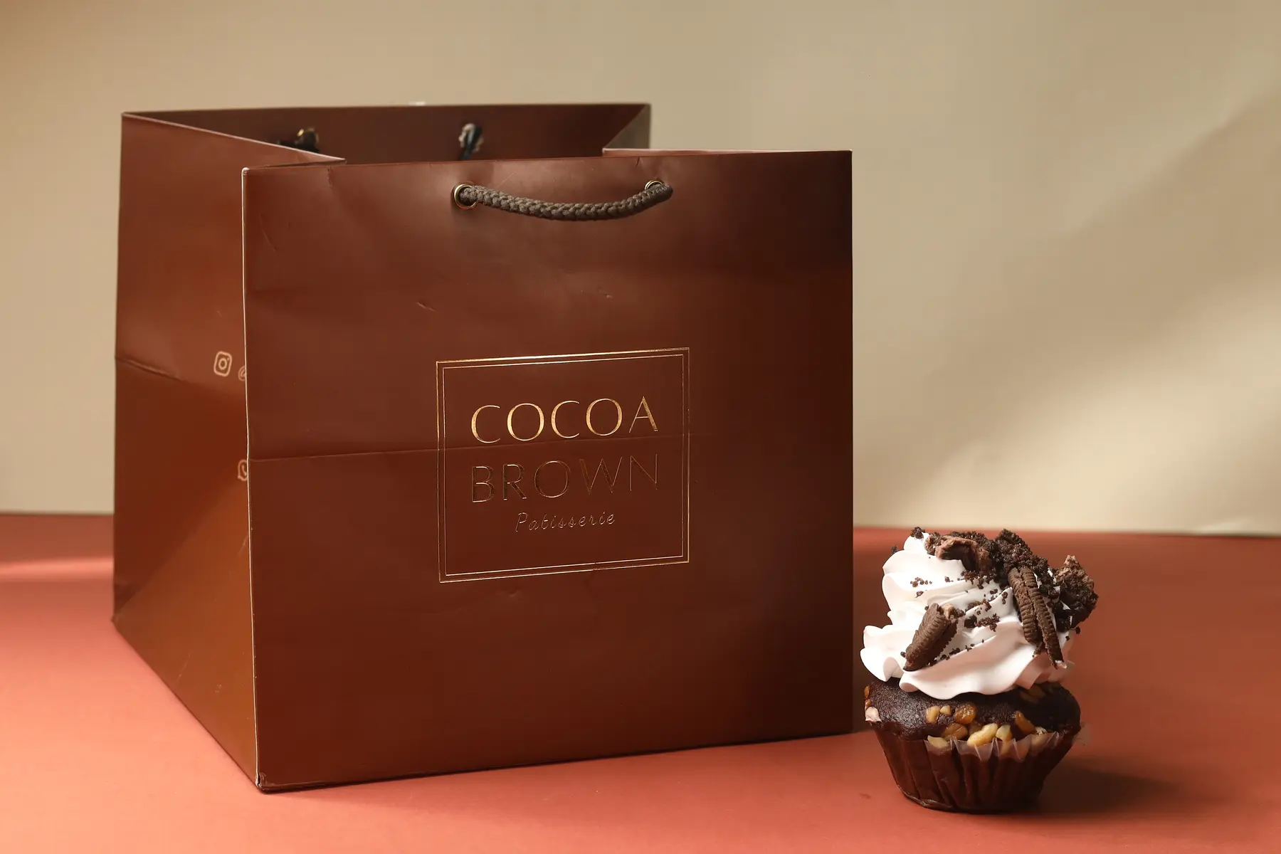 Premium brown paper bag with metallic print beside a small dessert