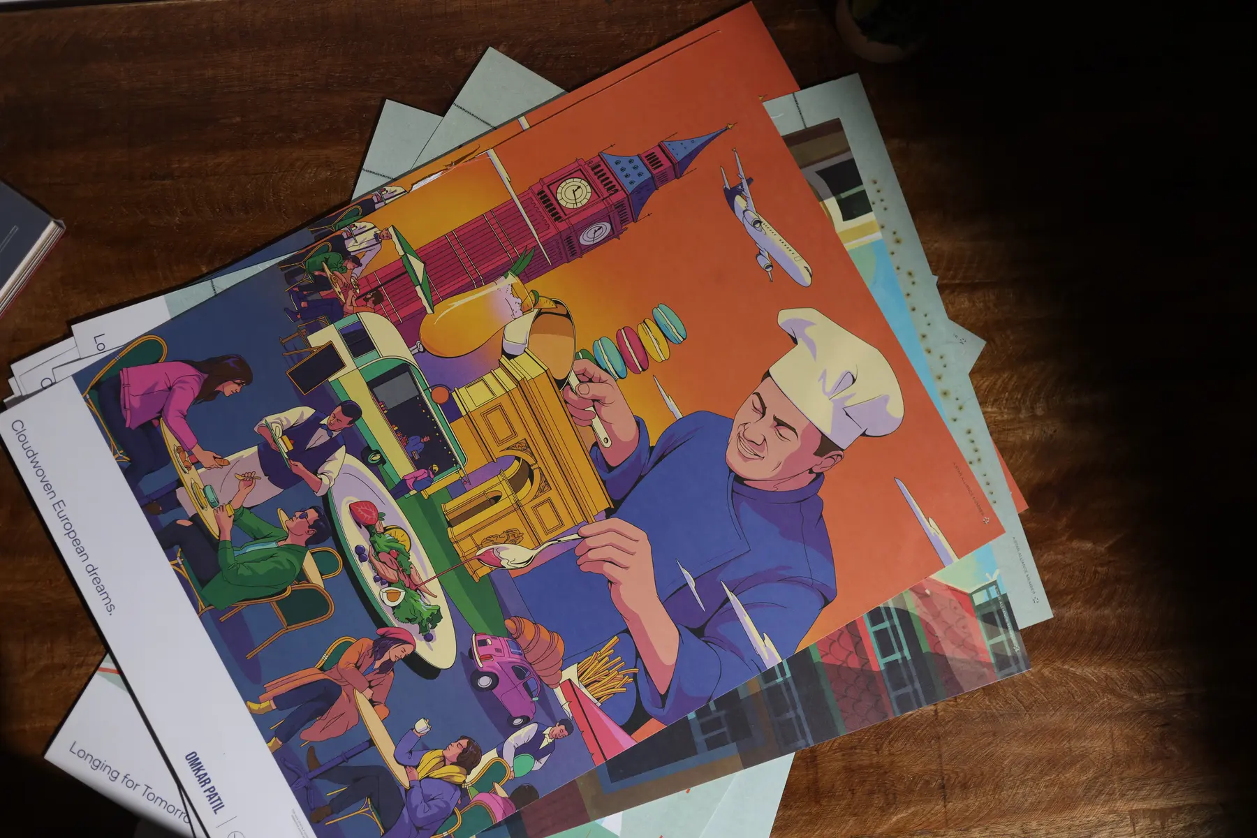 Stack of colourful illustrated art prints photographed on a wooden surface